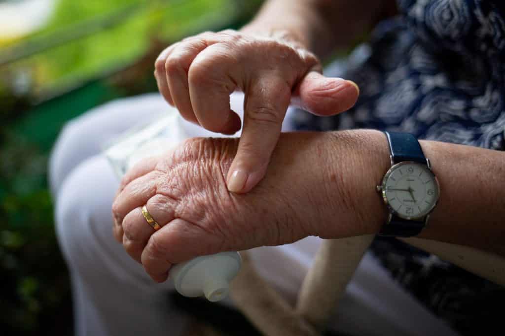 An elderly person's hands, using CBD oil on their skin.